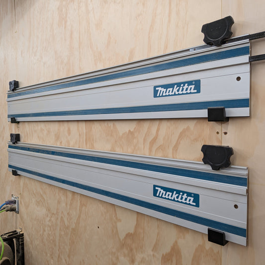 Two Makita wall-mounted aluminum rails with blue stripes and black knobs, installed on a plywood wall in a workshop setting.