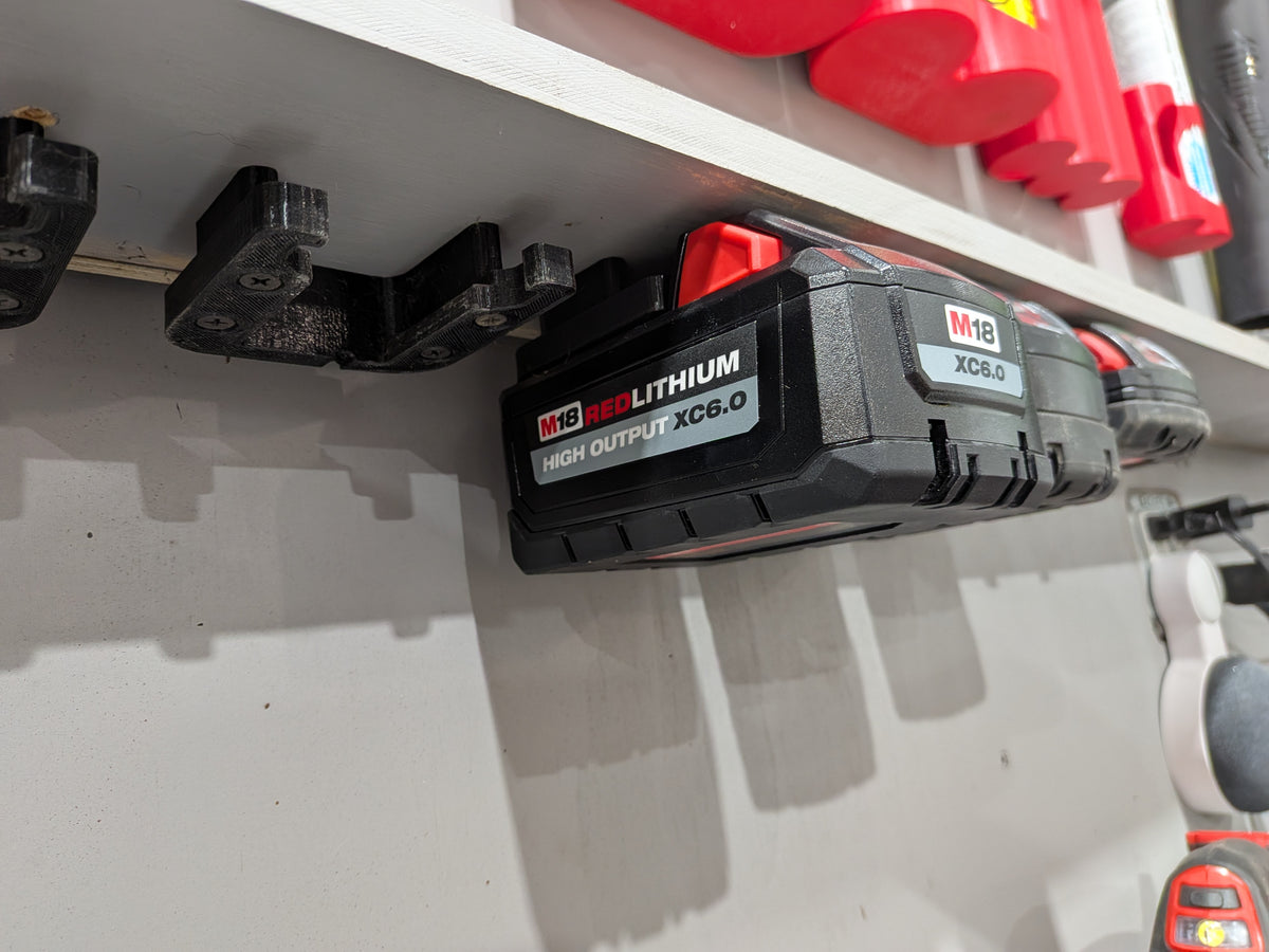 A RedLithium M18 high-output XC6.0 cordless battery mounted on a white wall shelf, with other tools partially visible in the background.