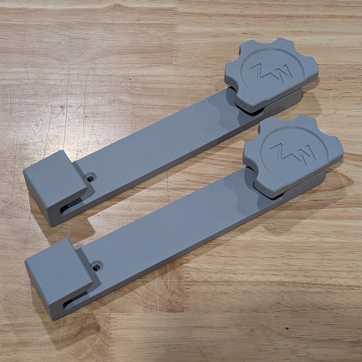 Two gray plastic tracksaw wall mounts with a gear-shaped end cap featuring an embossed 'ZW' logo, displayed on a light wood grain surface.