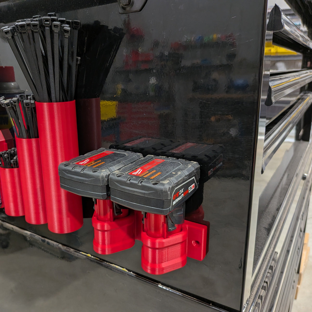Red magnetic tool holders mounted on a black metal toolbox, holding black zip ties and two cordless battery packs. A can of WD-40 is visible on the left.
