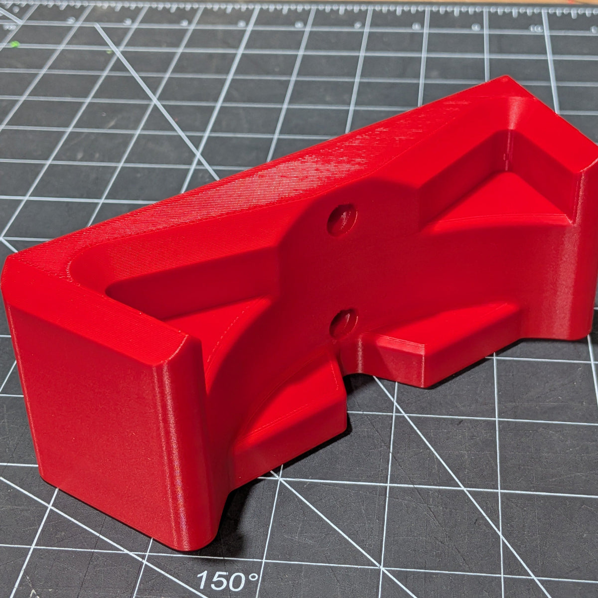 A bright red 3D-printed M18 Blower Mount with a matte finish, displayed on a dark gray gridded cutting mat.